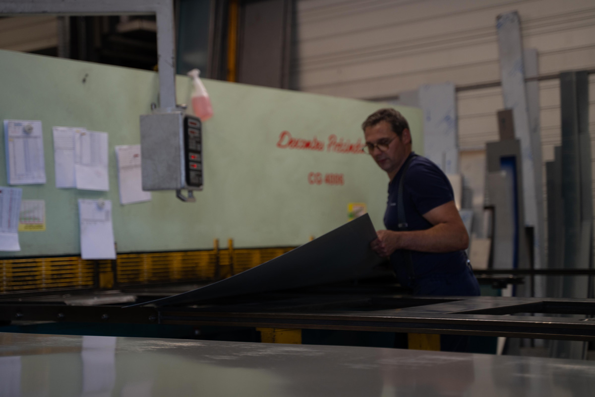 Homme manipulant une tôle métallique dans une usine.