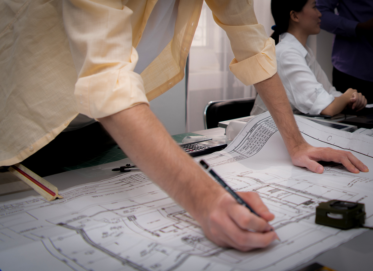 Architecte dessinant sur un plan technique.